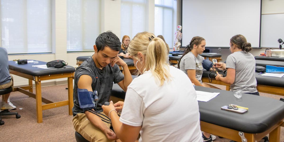 Students in a classroom paired up taking blood pressure.